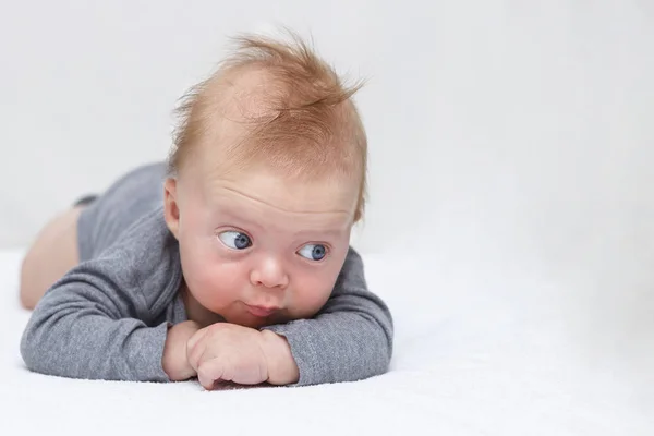 Bonito azul de olhos felizes bebê menino deitado na barriga e olhando para a câmera — Fotografia de Stock
