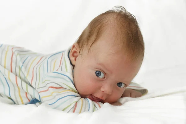 Bonito azul de olhos felizes bebê menino deitado na barriga e olhando para a câmera — Fotografia de Stock