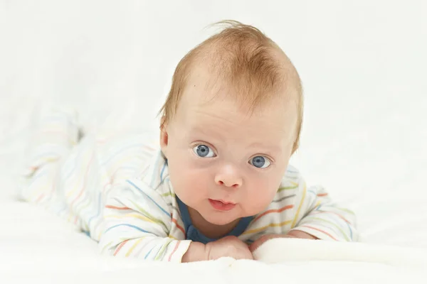 Bonito azul de olhos felizes bebê menino deitado na barriga e olhando para a câmera — Fotografia de Stock