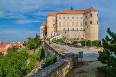 Mikulov, Çek Cumhuriyeti / South Moravia - 15 Ekim 2016: Mikulov kale sarı ve beyaz cephe ve kırmızı çatı ile ayakta duran bir kayanın üzerinde şehir manzarası, tuğla duvar, yeşil çalılar baskın