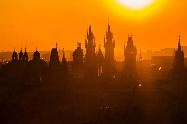 Hazy morning cityscape, orange and yellow sunrise in Prague, capital of the Czech Republic, sun shining above towers of Church of Our Lady before Tyn and silhouettes of spires and turrets