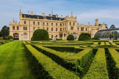 Lednice, Çek Cumhuriyeti - 27 Mayıs 2019: Güney Moravya'da sarı cepheli ünlü Lednice kalesi. Ön planda yeşil çim, çalı ve çiçek ile Bahçe. Güneşli bahar günü, mavi gökyüzü, beyaz bulutlar.