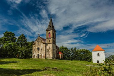 Krasikov, Kokasice / Çek Cumhuriyeti - 9 Ağustos 2019: Mecdelli Meryem'in eski kilisesinin ve bir çan kulesinin manzarası. Güneşli bir yaz günü. Yeşil çimenler, beyaz bulutlarla mavi gökyüzü.