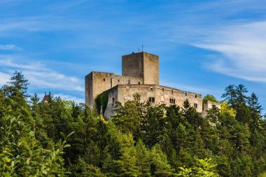 Çek Cumhuriyeti, Landstejn - 29 Eylül 2019: Ağaçlarla çevrili yeşil bir tepenin üzerinde duran taştan yapılmış bir ortaçağ şövalye kalesinin görüntüsü. Mavi gökyüzü ve beyaz bulutlarla aydınlık güneşli bir gün..