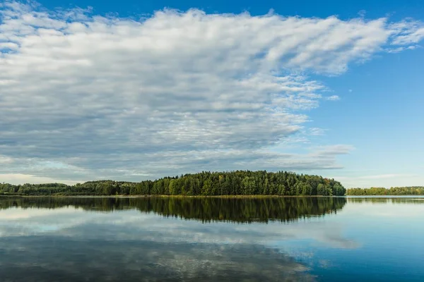 Eylül akşamı mavi gökyüzü, beyaz bulutlar, yeşil orman ve onun sakin sulardaki yansıması.