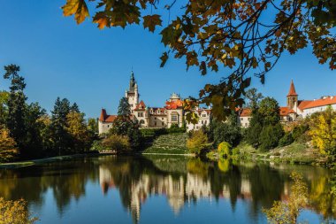 Pruhonice, Çek Cumhuriyeti - 7 Ekim 2019: Suya yansıyan ünlü romantik şatonun manzarası. Halka açık bir parkta tepede duruyor. Mavi gökyüzüyle güneşli bir sonbahar günü. 