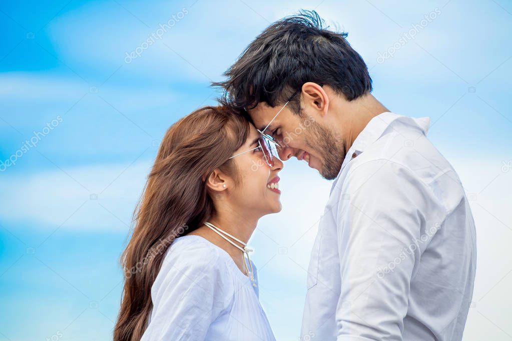 Young couple in love  looking to each other  and holding hand together at sea beach on blue sky .happy smiling young wedding with white dress kissing  Romantic moment head to head or face to face
