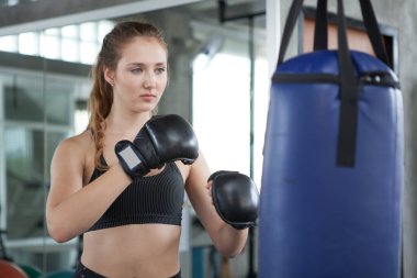 young fitness girl doing exercise hitting punching bag at a boxi clipart