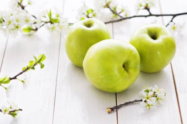 Olgun yeşil elma ile bahar çiçekleri Beyaz ahşap zemin üzerinde. Hafif yiyecekler arka plan, taze meyve, elma