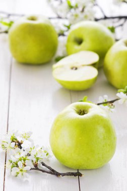 Beyaz ahşap zemin üzerinde bahar çiçekleri ile olgun yeşil elma.