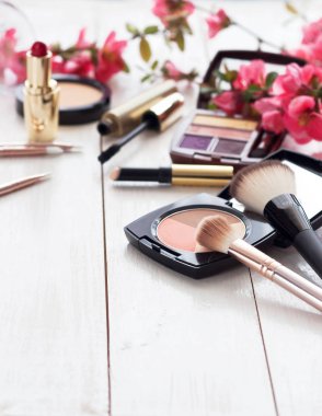 Kopya alanı ile beyaz ahşap zemin üzerinde pembe çiçekli makyaj için çeşitli kozmetik ürünleri. Kalıcı makyaj, ruj, rimel, göz farı, toz, fırçalar