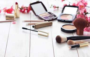 Kopya alanı ile beyaz ahşap zemin üzerinde pembe çiçekli makyaj için çeşitli kozmetik ürünleri. Kalıcı makyaj, ruj, rimel, göz farı, toz, fırçalar