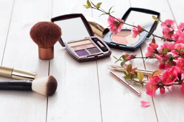 Kopya alanı ile beyaz ahşap zemin üzerinde pembe çiçekli makyaj için çeşitli kozmetik ürünleri. Kalıcı makyaj, ruj, rimel, göz farı, toz, fırçalar