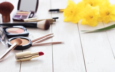 Kopya alanı beyaz bir ahşap zemin üzerine sarı nergis ile makyaj için çeşitli kozmetik ürünleri. Kalıcı makyaj, ruj, rimel, göz farı, toz, fırçalar