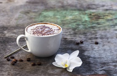 Bir fincan sıcak kahve ve orkide çiçek ahşap arka plan üzerinde. Geleneksel içki cappuccino veya kakao ahşap arka plan orkide çiçek sonbahar içki