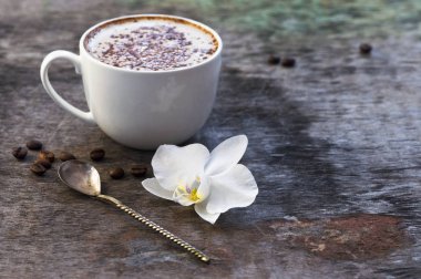 Bir fincan sıcak kahve ve orkide çiçek ahşap arka plan üzerinde. Geleneksel içki cappuccino veya kakao ahşap arka plan orkide çiçek sonbahar içki