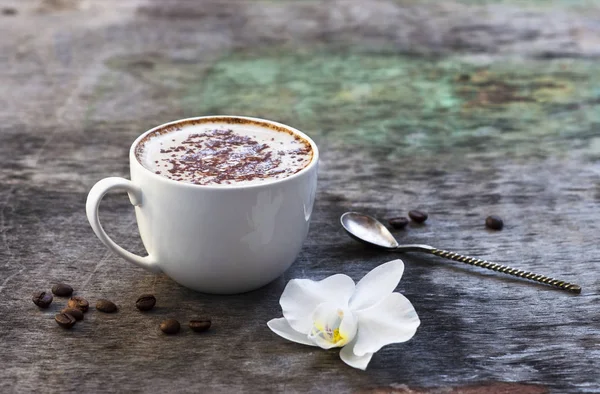 A cup of hot coffee and orchid flower on the wooden background. Traditional drink cappuccino or cocoa Wooden background Orchid flower Autumn drink
