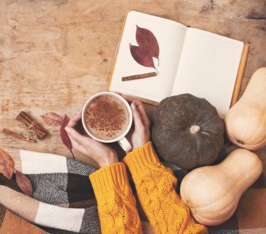 Kabak ve sonbahar yaprakları ile kırsal ahşap arka plan, Sütlü Balkabağı kahve veya kakao, defter, ekose bir kafes içinde bir kadının elleriyle, üstten görünüm etkisi tonda