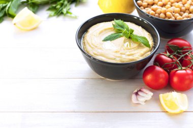 Humus, nohut, limon, kiraz domates ve beyaz rustik ahşap zemin üzerinde otlar ile top. Orta Doğu mutfağı. Arka plan humus