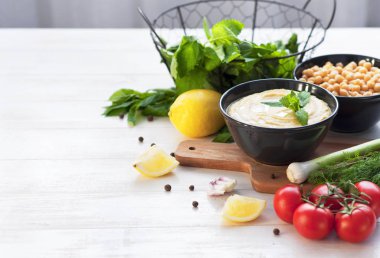 Humus, nohut, limon, kiraz domates ve beyaz rustik ahşap zemin üzerinde otlar ile top. Orta Doğu mutfağı. Arka plan humus