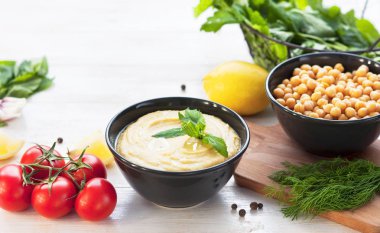 Humus, nohut, limon, kiraz domates ve beyaz rustik ahşap zemin üzerinde otlar ile top. Orta Doğu mutfağı. Arka plan humus
