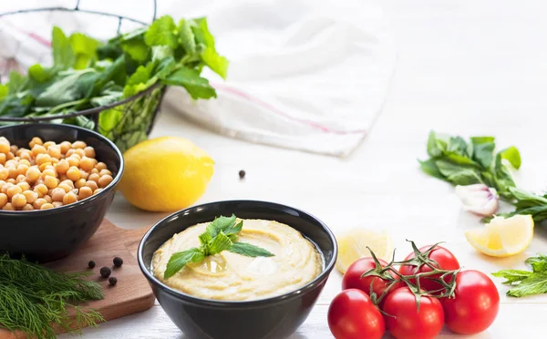 Humus, nohut, limon, kiraz domates ve beyaz rustik ahşap zemin üzerinde otlar ile top. Orta Doğu mutfağı. Arka plan humus