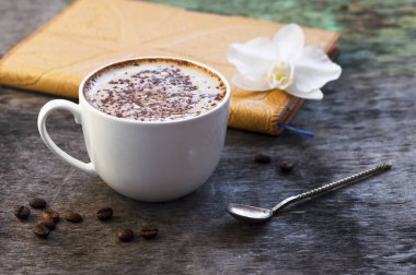 Bir fincan sıcak kahve ve ahşap arka plan üzerinde bir günlük ile bir orkide çiçeği. Cappuccino veya kakao ahşap arka plan orkide Not defteri günlüğü sonbahar içki geleneksel içki