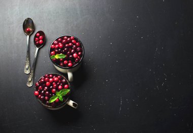 Kopya alanı bir koyu siyah zemin üzerine beyaz bir bardak ve kaşık nane yaprakları ile taze kırmızı kızılcık. Berry, tatil Noel arka plan