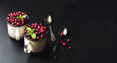 Kopya alanı bir koyu siyah zemin üzerine beyaz bir bardak ve kaşık nane yaprakları ile taze kırmızı kızılcık. Berry, tatil Noel arka plan
