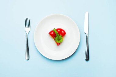 Bir beyaz tabak, çatal ve bıçak, diyet, sağlıklı gıda kavramı kırmızı biber. Taze biber, sağlık. Gıda yaratıcı kavramı. Üstten görünüm mavi arka plan düz koymak kopya alanı minimalist tarzı ile