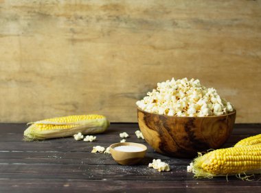 Kahverengi ahşap kase lezzetli geleneksel patlamış mısır, taze mısır ve koyu ahşap arka plan üzerine bir kaşık ile. Üstten görünüm bir hafif yemek arka plan. Mısır yemekleri