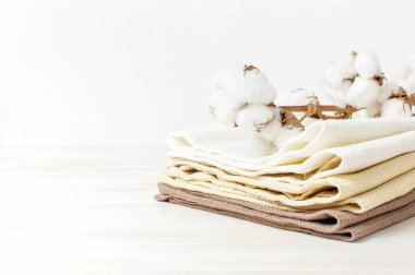 Multicolored clean towels with a branch of cotton on a light wooden background with copy space. Texture of cotton, waffle towel, textiles. Towels for kitchen or Spa concept. Isolated object clipart