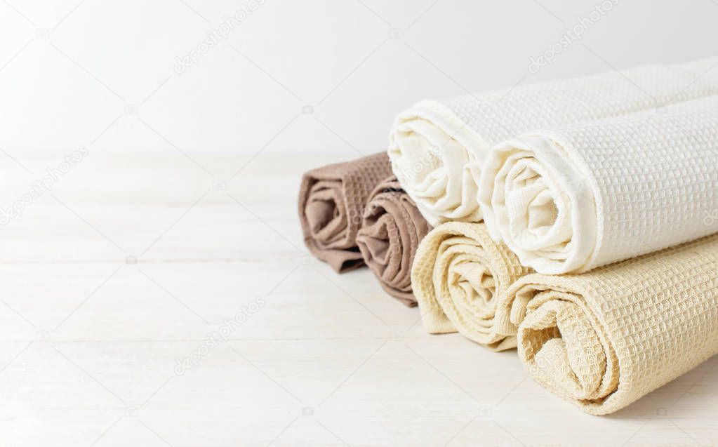 Multicolored clean towels on a light wooden background with copy space. Texture of cotton, waffle towel, textiles. Towels for kitchen or Spa concept. Isolated object