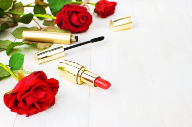 Kopya alanı beyaz bir ahşap zemin üzerine kırmızı güllü makyaj için çeşitli kozmetik ürünleri. Makyaj aksesuarlar kırmızı ruj siyah rimel seçici odak. Kadınsal