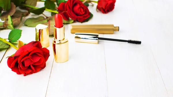 Various cosmetic products for make-up with red roses on a white wooden background with copy space. Makeup Accessories Red lipstick Black mascara Selective focus. Women\'s things