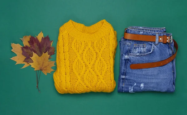 Turuncu erkek örgü kazak, kot ve sonbahar yaprakları koyu yeşil arka plan üstüne düz lay görüntüleyin. Moda Bayan giyim ayarla Trendy rahat örgü Jumper sonbahar aksesuarları bayan moda bakmak