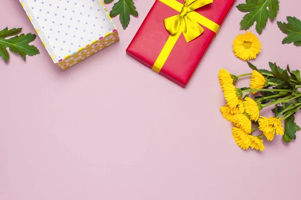 Red gift box with gold ribbon and yellow chrysanthemums on pink background top view flat lay. Holiday concept, birthday gift valentine day or anniversary. Congratulations background copy space.