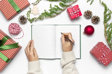 Örme kazak kadın elinde kalemiyle temiz defter planları için yeni yıl hediye kutuları, beyaz masa düz dallarda köknar yatıyordu yazıyoruz. Noel planlama kavramı tatil dekorasyon 2019 gol