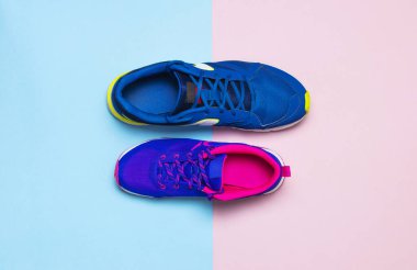 Blue mens and violet-pink female sneakers on pastel pink and blue background flat lay top view with copy space. Sports shoes, fitness, concept of healthy lifestile everyday training. clipart