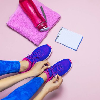 Mavi tozluk spor genç kadın spor ayakkabı, eğitim için hazırlanıyor verdi. Pastel pembe arka plan düz üstünde su havlu defter spor şişe için aksesuarlar üstten görünüm yatıyordu. Fitness kavramı