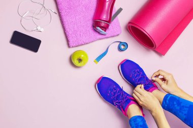 Genç kadın mavi spor ayakkabı içinde elma elinde, eğitim için hazırlanıyor tutar. Şişe su, yoga mat, telefon, pastel pembe arka plan düz kulaklıktan üstten görünüm yatıyordu. Spor ayakkabı Fitness kavramı
