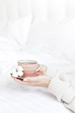 Beyaz örgü kazak kadınlar elinde fincan çay tabağı ile hassas pamuk çiçek yatakta üzerinde tutun. Rahat sabah kahvaltı evde yaşam tarzı nazik arka plan kopya alanı sonbahar kış kavramı