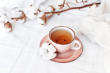 Bir fincan sıcak çay, hassas pamuk ve beyaz keten ile yatakta ekose kazak örme dalı. Rahat sabah kahvaltı evde yaşam tarzı nazik kadın arka plan kopya alanı sonbahar kış kavramı