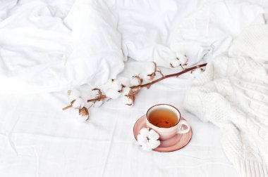 Bir fincan sıcak çay, hassas pamuk ve beyaz keten ile yatakta ekose kazak örme dalı. Rahat sabah kahvaltı evde yaşam tarzı nazik kadın arka plan kopya alanı sonbahar kış kavramı