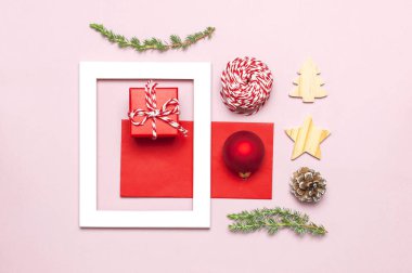 Noel kompozisyon. Beyaz fotoğraf çerçevesi, kırmızı zarf, çam dalları, koniler, top, sicim, Hediyelik, pembe bir arka plan düz Ahşap oyuncaklar üstten görünüm yatıyordu. Noel Kış dekorasyonu yeni yıl, tatil nesneleri