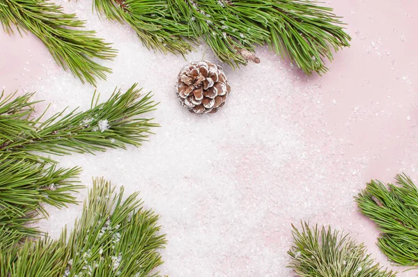Fond de Noël, branches de pin vert, cônes décorés de neige sur fond rose neigeux. Composition créative avec bordure et espace de copie design vue de dessus. Nouvel An, vacances, décoration — Photo
