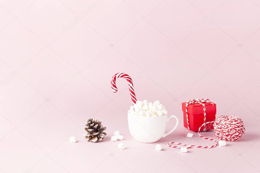 White mug with marshmallows Candy Cane, red gift box, pine cone, decorative lace on pink background Flat Lay Winter traditional drink food Festive decor Christmas New Year presents Xmas holiday