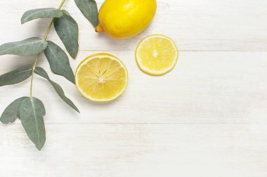 Bütün ve dilimlenmiş taze limon, okaliptüs Beyaz ahşap zemin üzerine bırakır. Yat, görünümü, kopya alanı top. Çok az meyve konsept tasarımı. Sarı narenciye limon