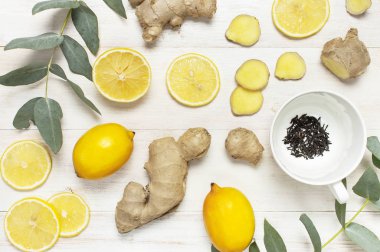 Fresh ginger root, cup tea with brewing inside, lemon, eucalyptus leaves on white wooden background. Flat lay, top view, copy space. Minimalistic style, seasoning, spice ingredient for tea. clipart