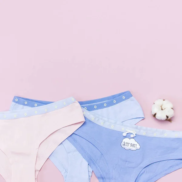 Female pastel cotton set panties and cotton flower on pink background top view flat lay with copy space for text. Fashion blog, Colorful women's natural underwear, advertising shopping concept.